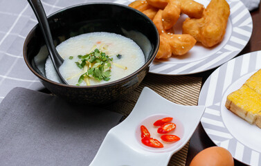 Chinese style porridge or porridge and fried dough stick or fried dough stick or donut or fried bread placed on a brown wooden table. Thai street food called "Porridge" and "Patongko", and toast