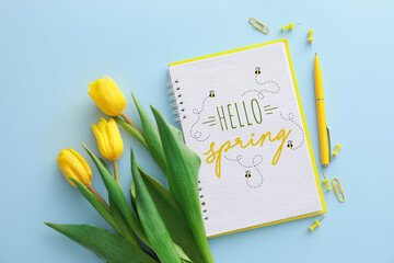 Notebook with text HELLO SPRING, yellow tulip flowers and stationery on blue background