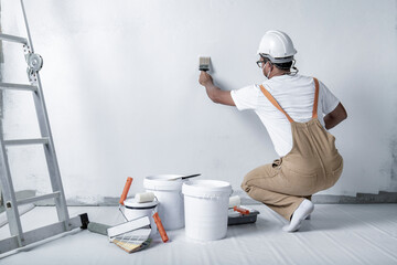 a man paints a white wall with a roller. Repair of the interior. Young male decorator painting a...