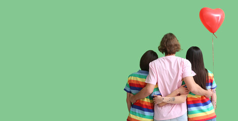 Man and two beautiful women in rainbow clothes and with balloon on color background with space for...