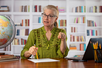 Portrait of remote teacher woman talking looking at webcam point of view in home office library. Teaching students doing video chat. Remote learning concept.