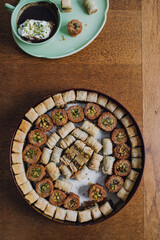 Top down shot of assorted circular tin of middle eastern baklava filo dough pastry sweets with hot chocolate