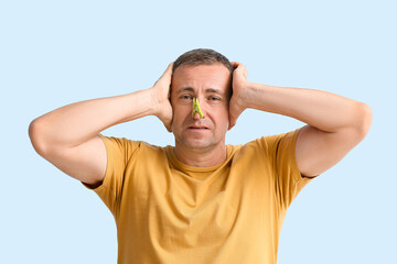 Stressed ill mature man with clothespin on his nose against color background