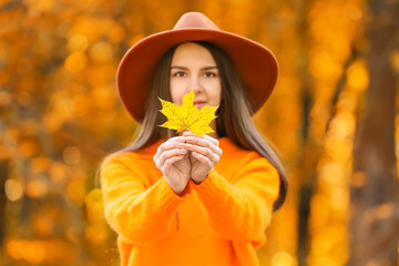 Young woman holding golden autumn leaf in park