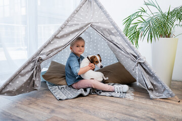 Kid hugging jack russell terrier in tepee at home.