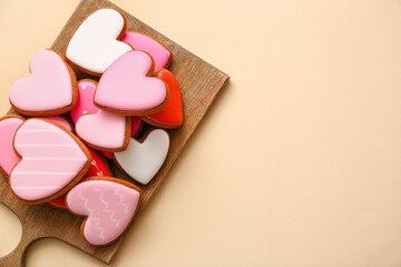 Wooden board with tasty heart shaped cookies on beige background