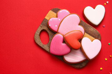 Obraz na płótnie Canvas Wooden board with tasty heart shaped cookies on red background