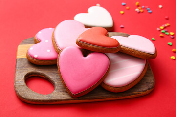 Wooden board with tasty heart shaped cookies on red background