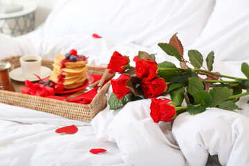 Bouquet of roses, wicker tray with delicious breakfast and gift for Valentine's Day on bed