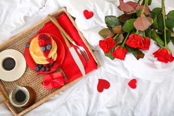 Bouquet of roses, wicker tray with breakfast and gift for Valentine's Day on bed