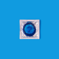 Blue condom in transparent package against blue background.