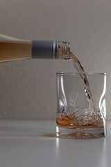 First glass of wine being poured from a full bottle of wine . Gray background and table. Bubbles forming on the top of the liquid.