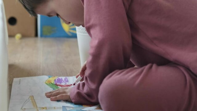 Video with a boy drawing with pencils, sitting on the floor of the house. Distance education.