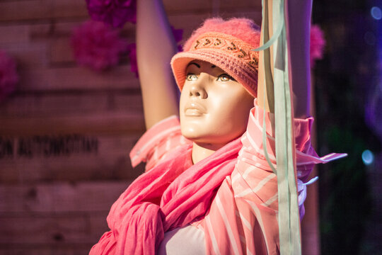 Close-up of mannequin with arms raised wearing a wool hat, shirt and a sweater tied around the neck. All in pink tones.