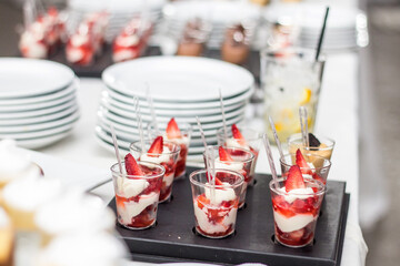 Mesa dulce en fiesta de 15, boda, cumpleaños o evento.  Primer plano de copas individuales de mini postres con crema y frutillas o fresas, fondo desenfocado con postres variados.