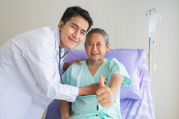 Elderly patient man looking to camera with happyness and showing thumbs and doctor using stethoscope on heart. Doctor or nurse take care senior patient health admission at hospital