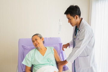 Obraz premium Elderly patient man sit on bed and look away from syringe in hand of doctor with unhappy, ache, sad, suffer from syringe. Doctor or nurse take care senior patient health admission at hospital