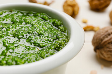 Bowl of tasty pesto sauce and walnuts on light wooden background