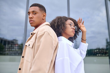 Man and woman standing back to back on street