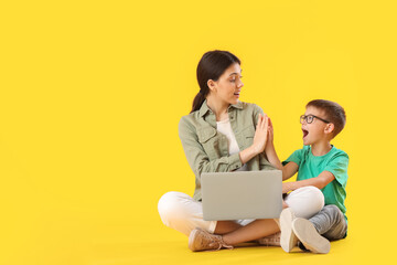 Little boy and his older sister with laptop giving each other high-five on yellow background