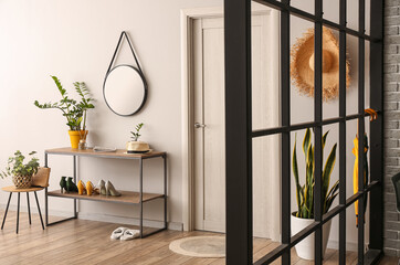 Stand for shoes, mirror and houseplants near light wall in hallway - obrazy, fototapety, plakaty