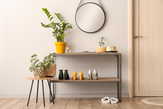 Stand with shoes, mirror and houseplants near light wall in hallway