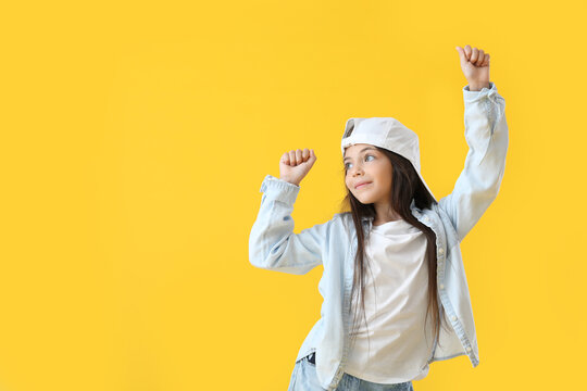 Adorable little girl in cap dancing on yellow background