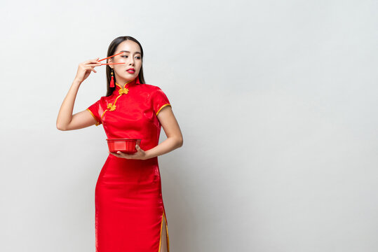 Asian woman in traditional red dress raising arm with chopsticks and looking at copy space aside  against gray background