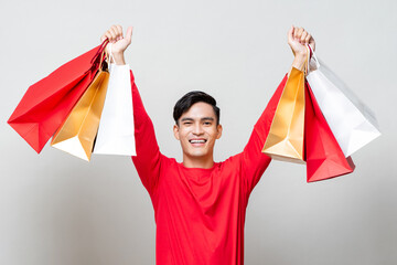 Surprised Asian man raising hands showing shopping bags in isolated light gray studio background...