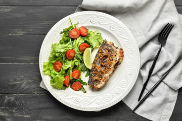 Plate with delicious sea bass fish, vegetables and cutlery on dark wooden background