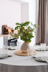 Dining table with setting and vase with autumn branches in kitchen