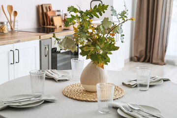 Dining table with setting and vase with beautiful autumn branches in kitchen
