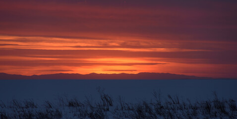 Red sunset against the backdrop of distant mountains in winter