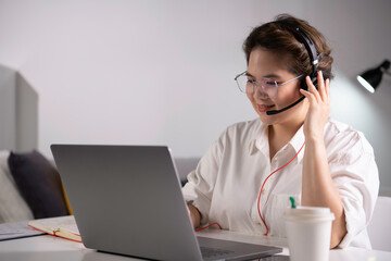 Feeling good happy and positive at work. Young Asian businesswoman wearing headset on video call with clients on laptop. Young Asian woman giving online educational class lecture, consulting customer.