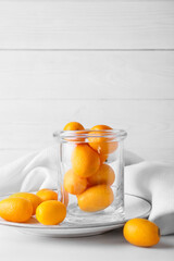 Jar with tasty kumquat fruits on light wooden background