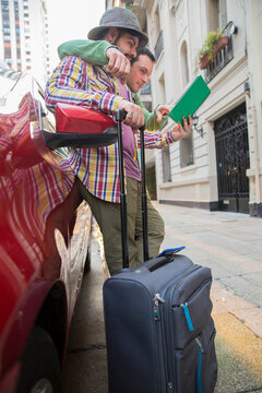 A Latin Gay Tourist Couple On A Red Car Looking For Directions In The City Enjoying Vacations. Vertical Frame. 