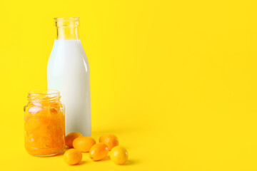 Jar of tasty kumquat jam and bottle with milk on yellow background