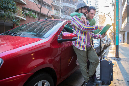 A Latin Gay Tourist Couple On A Red Car Looking For Directions In The City To Celebrate A Romantic Getaway Trip.