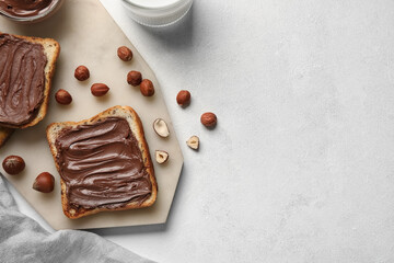 Board of bread with chocolate paste and hazelnuts on white background, closeup