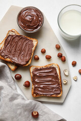 Bread with chocolate paste, hazelnuts and glass of milk on white background