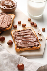 Board of bread with chocolate paste and hazelnuts on white background