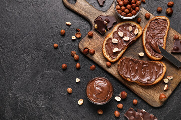 Wooden board of bread with chocolate paste and hazelnuts on black background