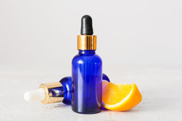 Bottles of essential oil and fresh orange on light background, closeup