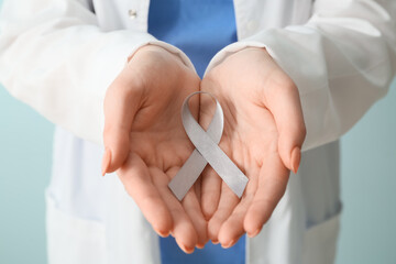 Female doctor with Parkinson's awareness ribbon on light background, closeup