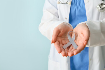 Female doctor with Parkinson's awareness ribbon on light background, closeup