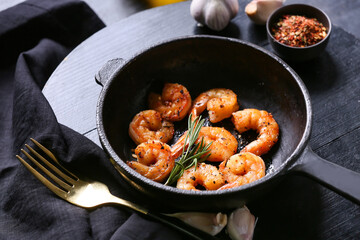 Frying pan of tasty shrimp tails on black background