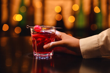Female hand with tasty Manhattan cocktail on table in bar