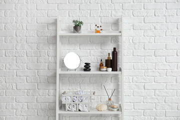 Shelving unit with bath supplies near white brick wall