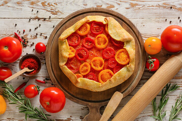 Board with tasty tomato galette on light wooden background