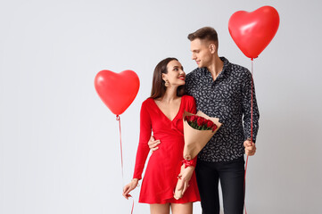 Happy young couple with bouquet of flowers and balloons on light background. Valentine's Day celebration